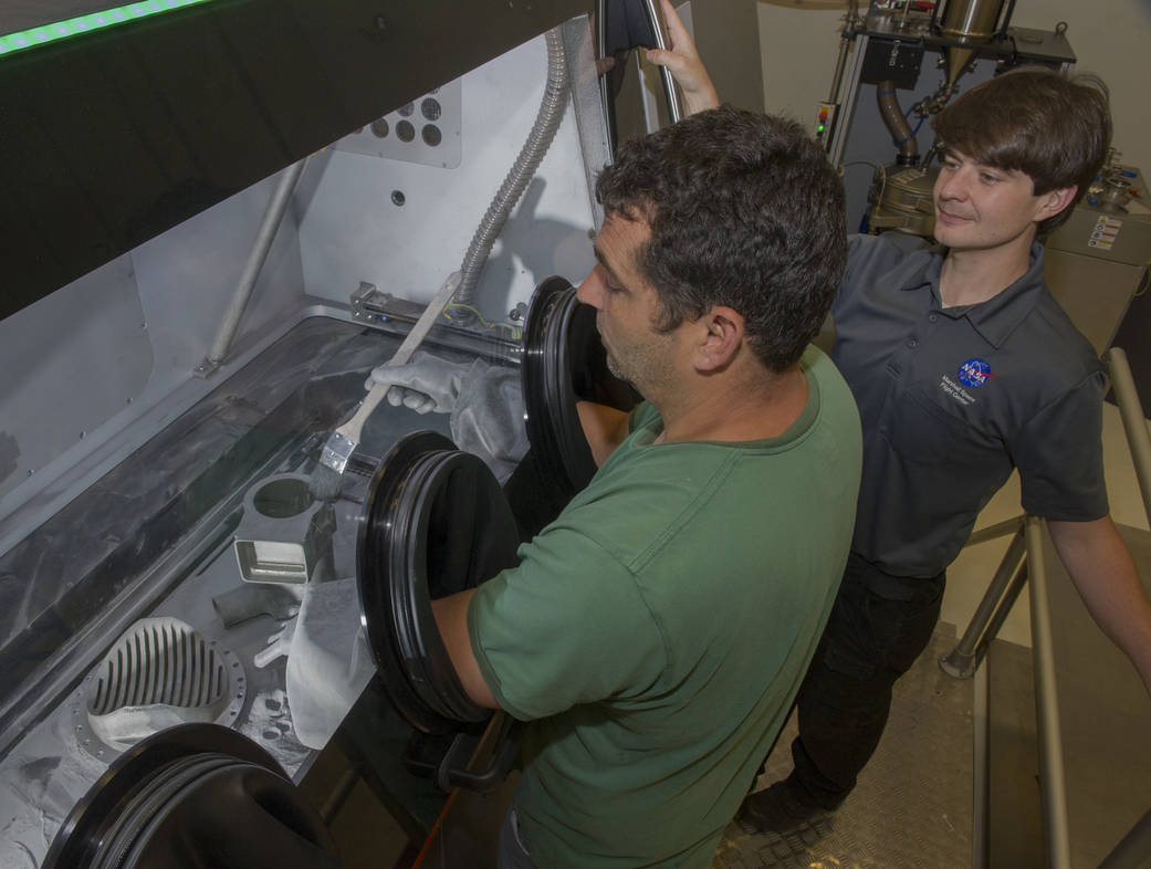 Marshall Center engineers Jim Lydon, left, and Zach Jones work on a recently 3-D printed rocket part.