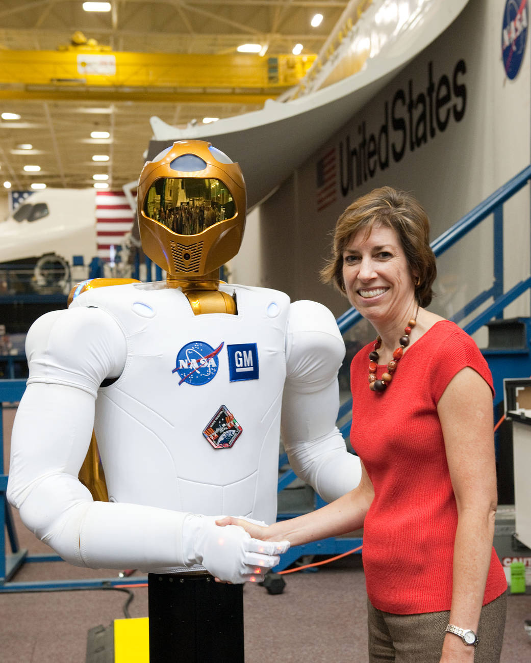 Ellen Ochoa (left) shakes hands with Robonaut 2 in the Space Vehicle Mock-up Facility.