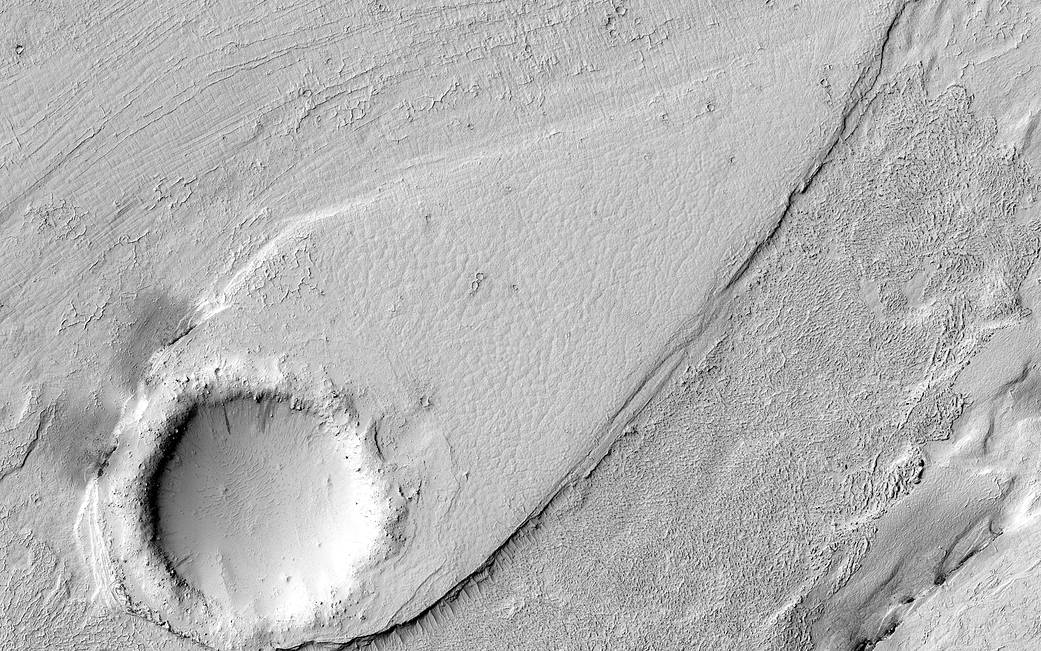 Gray circular form at lower left with channel of dune on Mars surface
