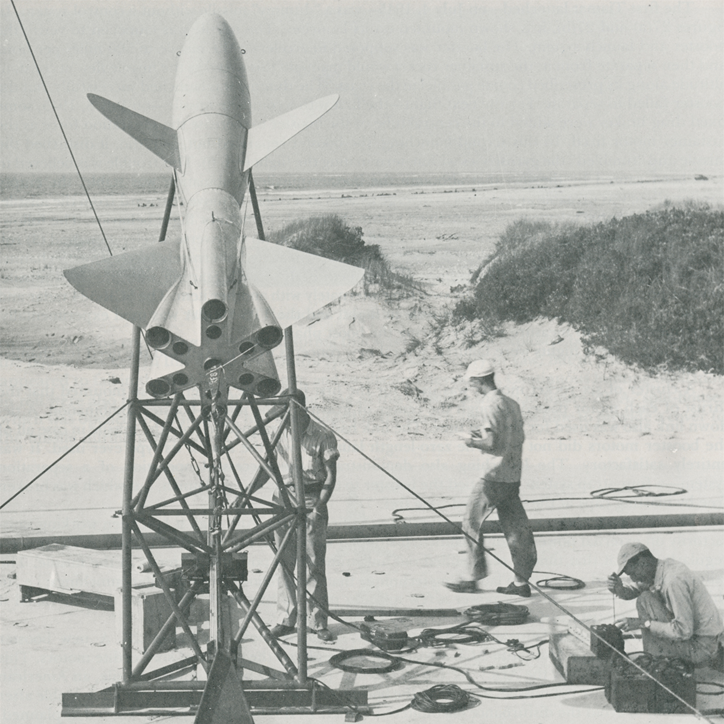 Black and white image of a rocket on a metal structure with people working around it.