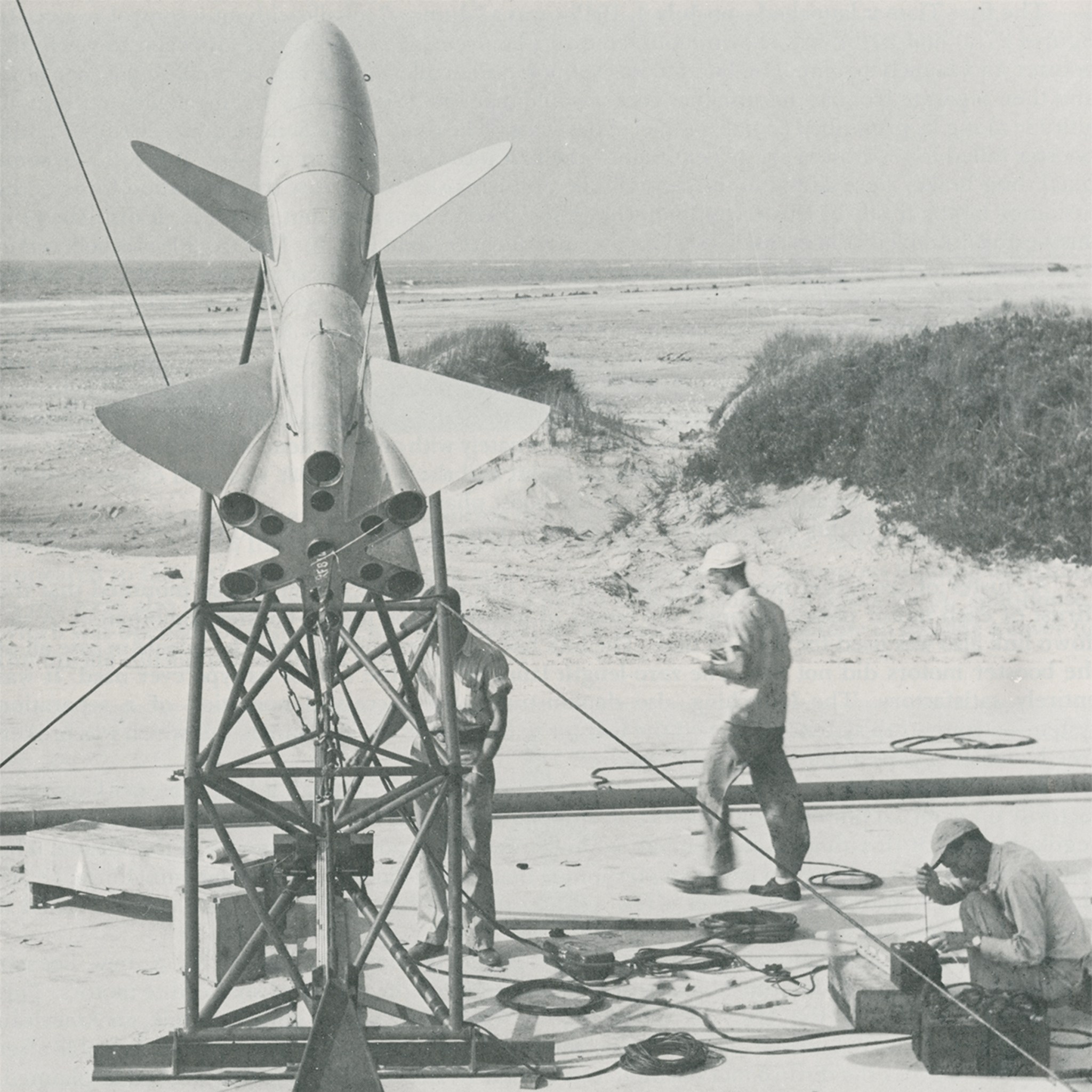 Black and white image of a rocket on a metal structure with people working around it.
