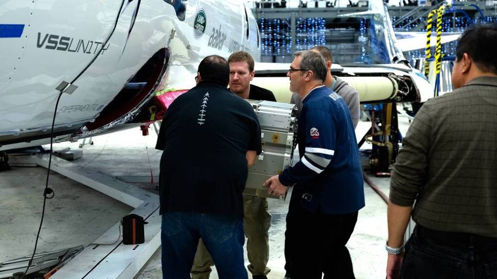 Four men loading a technology payload onto ShpaceShipTwo.