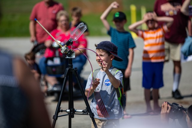 A small child prepares to launch a bottle rocket that's on a tripod.