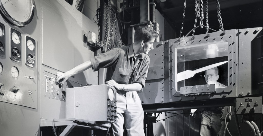 Two men look at model in wind tunnel test section.