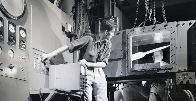 Two men look at model in wind tunnel test section.