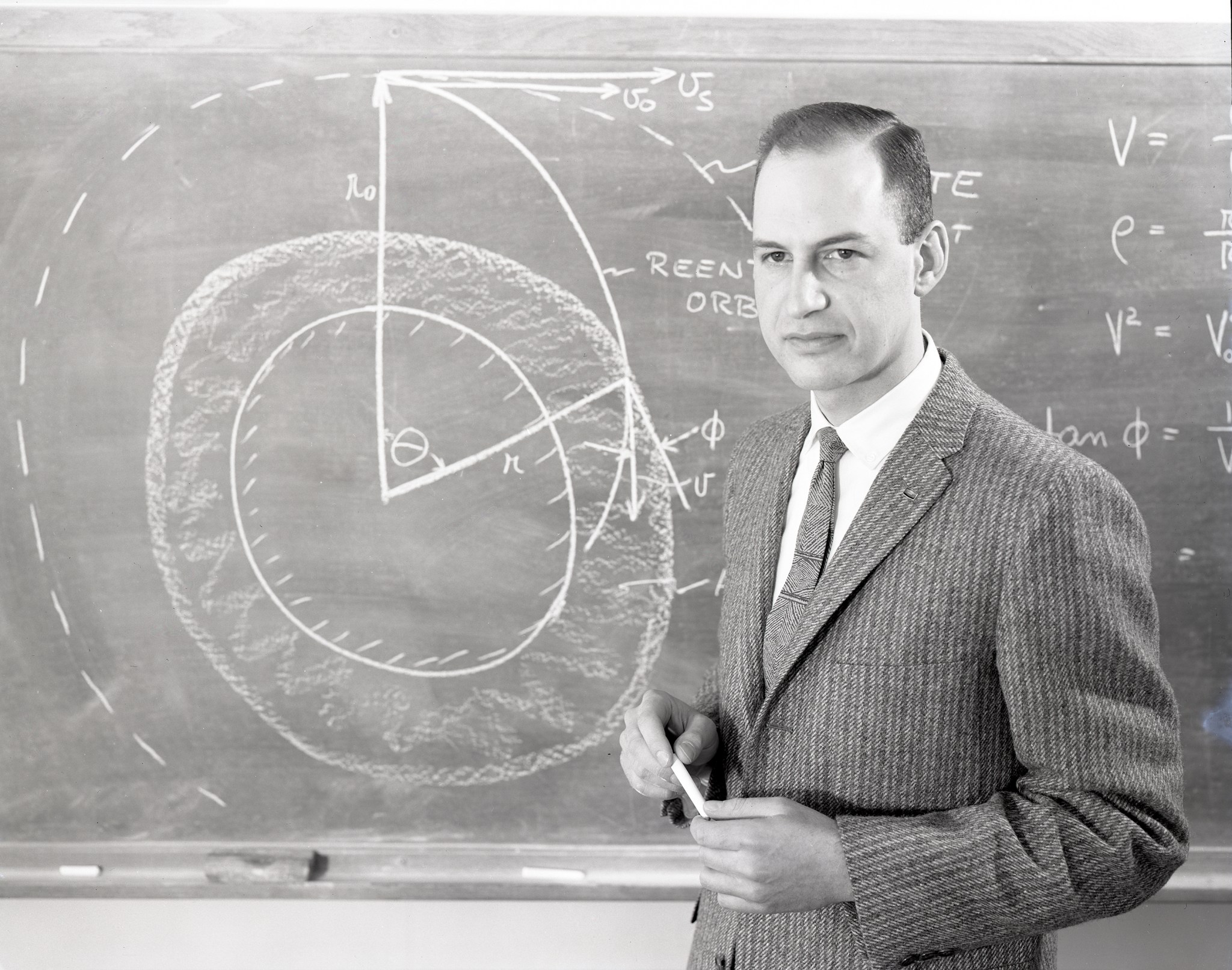 George Low in front of blackboard with calculations.