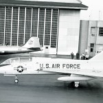 Two military aircraft in front of hangar.