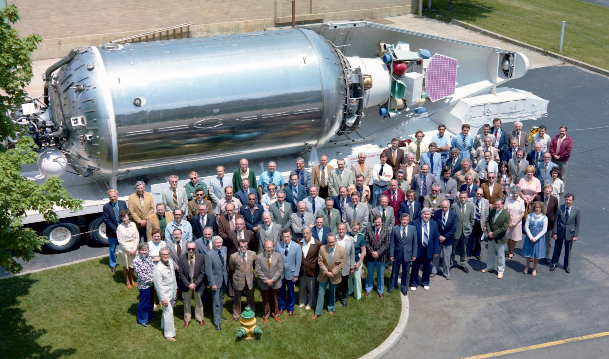 Group of people standing in front of horizontally-mounted rocket.