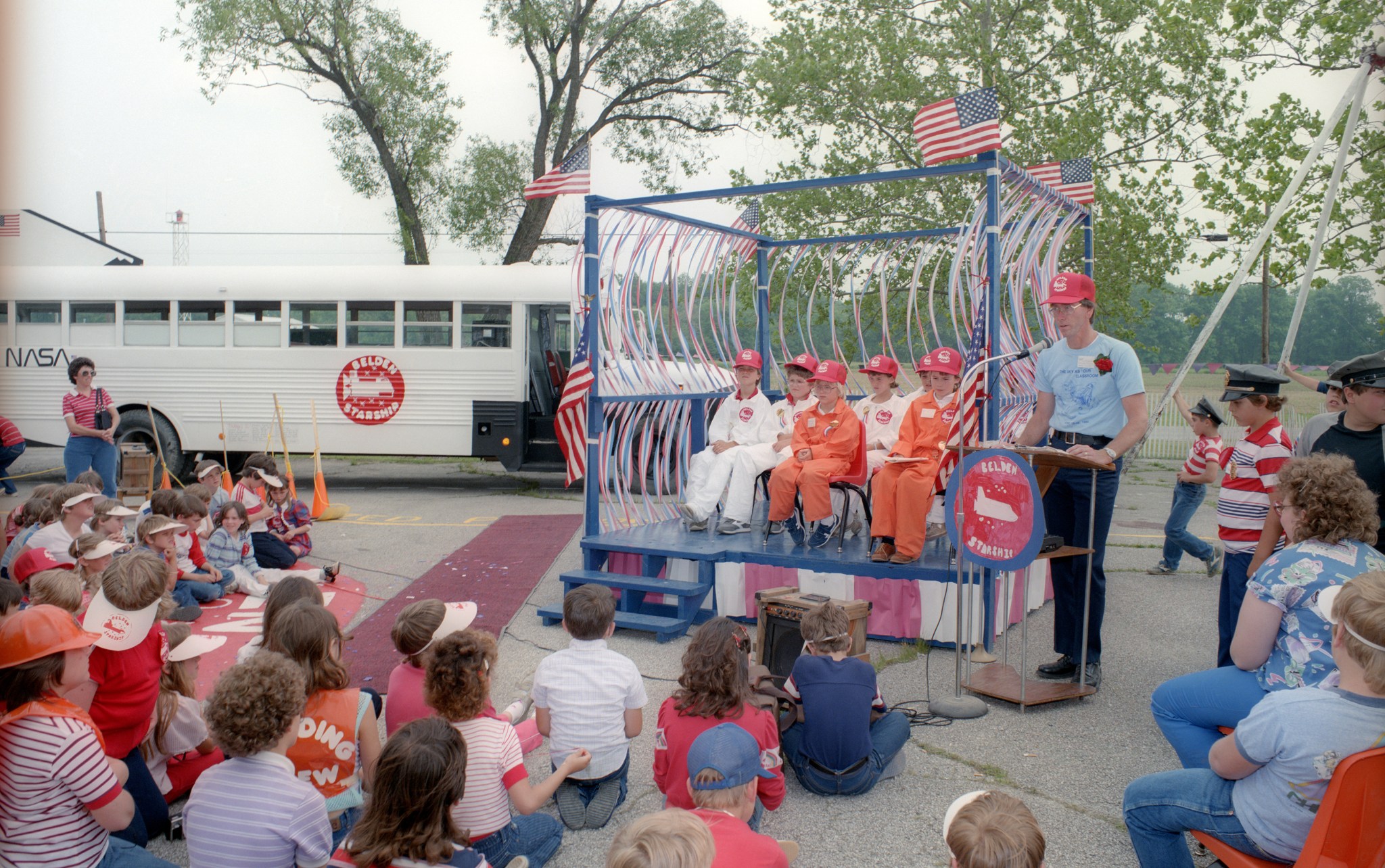 Students on outdoor stage with bus in background.