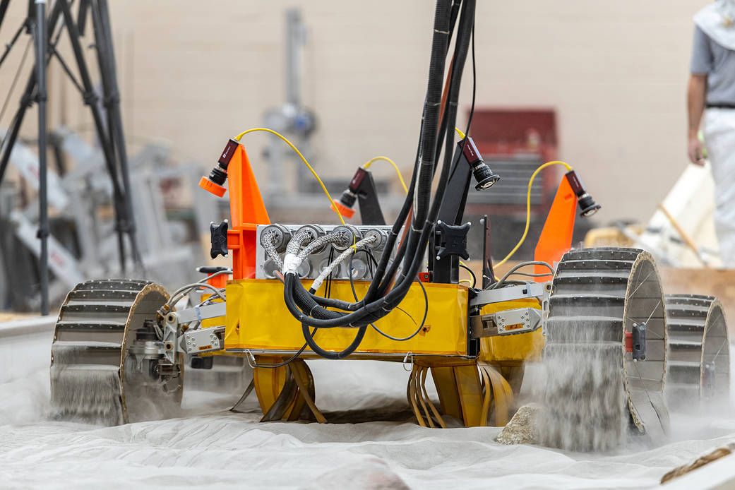 A yellow robotic rover kicks up sand in a mobility test bin.