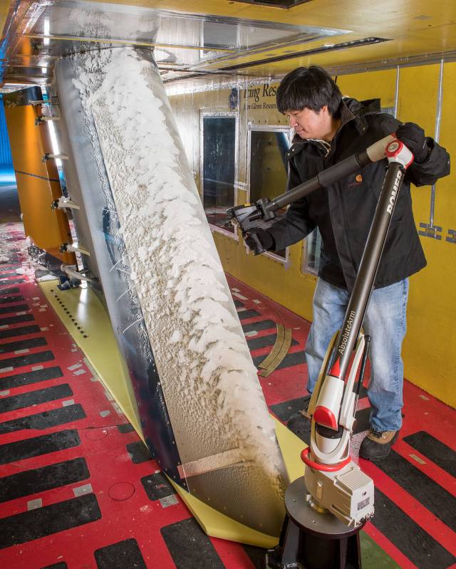 Man wears a winter coat, standing inside the Icing Research Tunnel with an instrument to measure the ice buildup on an aircraft component. 
