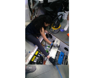 HERA crew member Monique Garcia inspects tanks and wires beneath a floor panel of a habitat that NASA uses to simulated space missions.