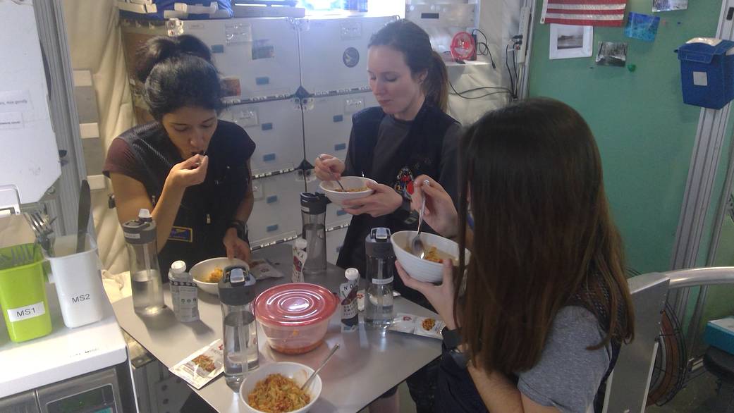 HERA crew members Monique Garcia, Lauren Cornell, and Madelyne Willis dine together at the kitchen table.