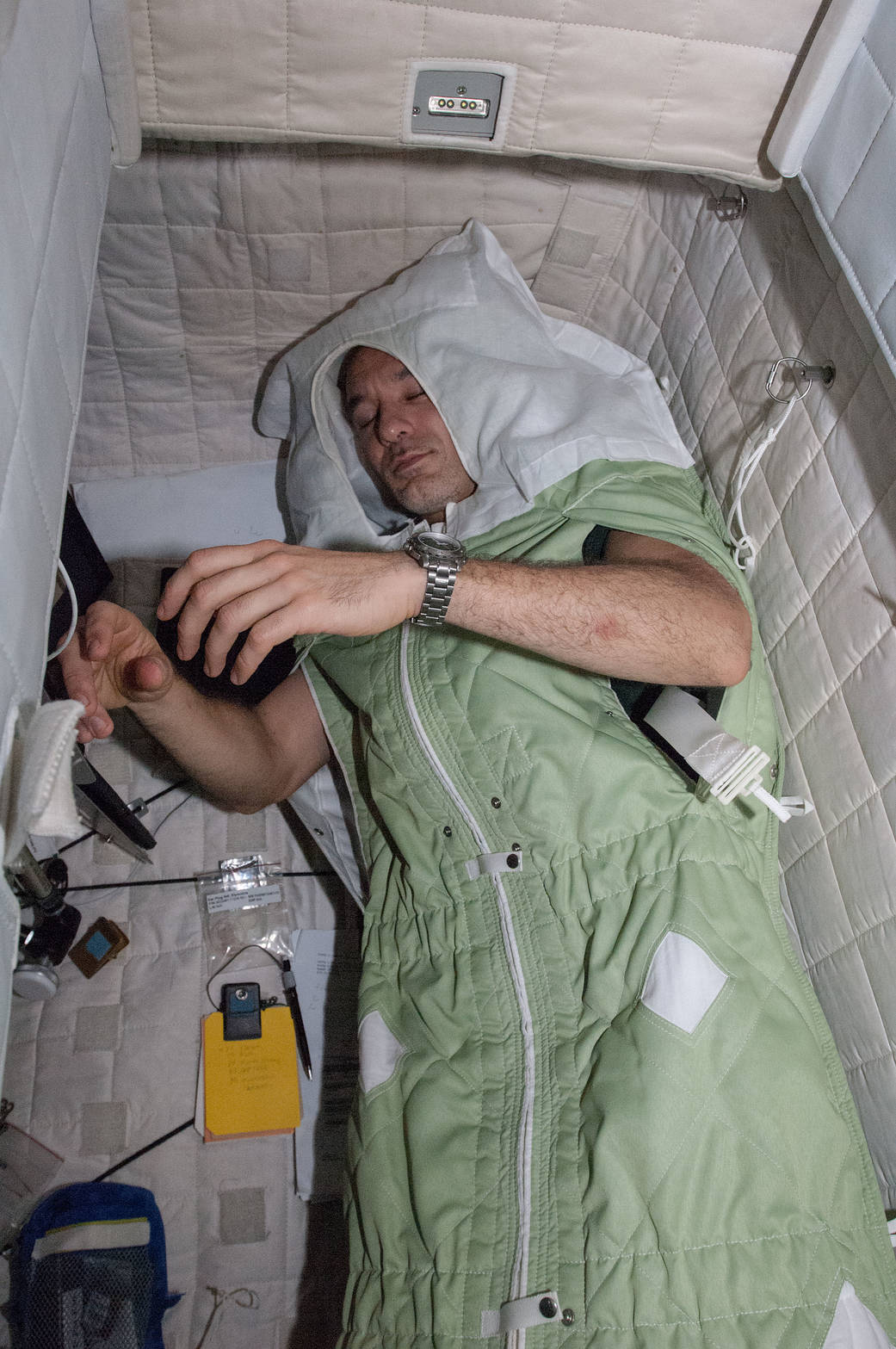 View of an ISS crewmember wearing a sleep restraint in his crew quarters.