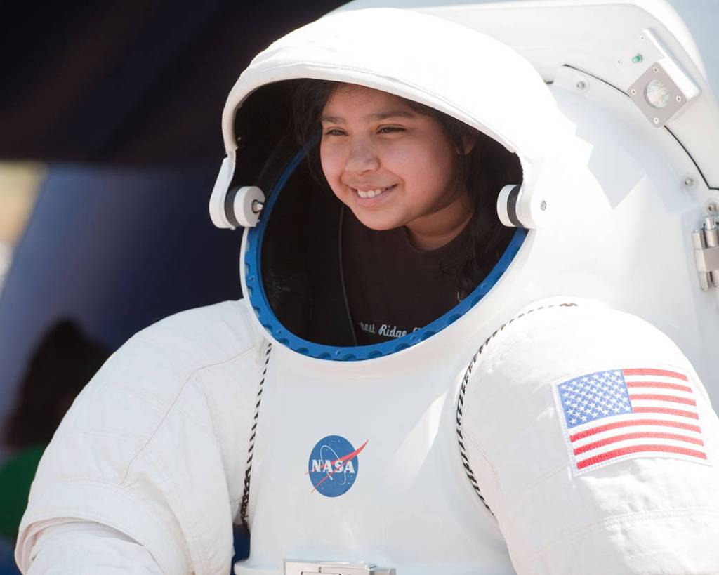 A student peeks out from under a demonstration EVA suit at a MX:TLA event