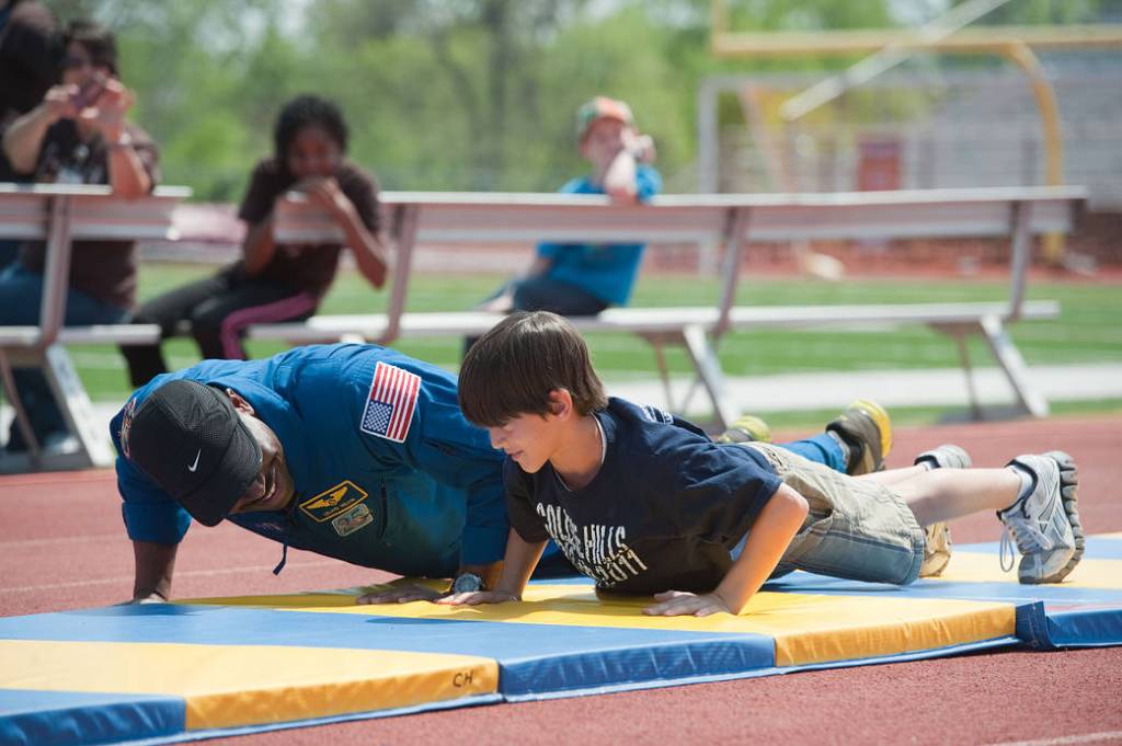An astronaut and a boy do push-ups side-by-side