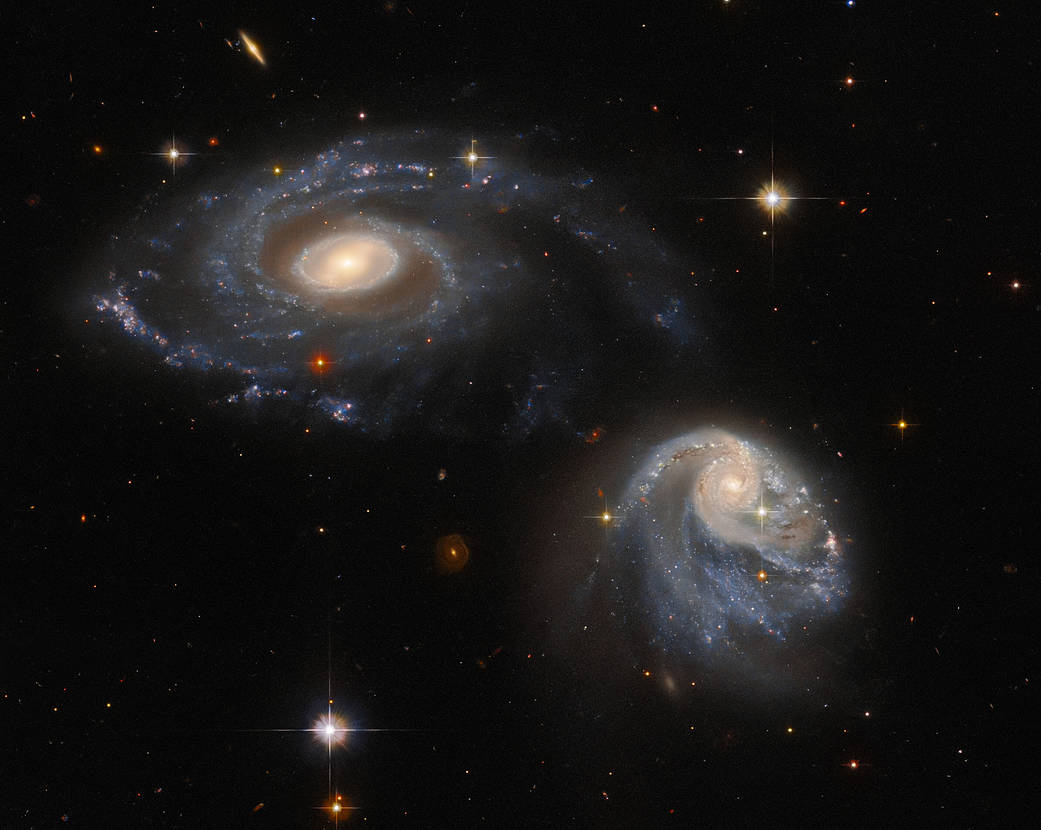 two spiral galaxies, one at upper-left the other at lower-right, both are nearly face-on providing views of their spiral arms, background stars and galaxies 