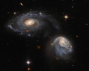 two spiral galaxies, one at upper-left the other at lower-right, both are nearly face-on providing views of their spiral arms, background stars and galaxies