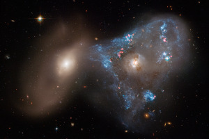 Two galaxies, one on the right and one on the left. The right galaxy has a blue-white triangular star forming region surrounding it.