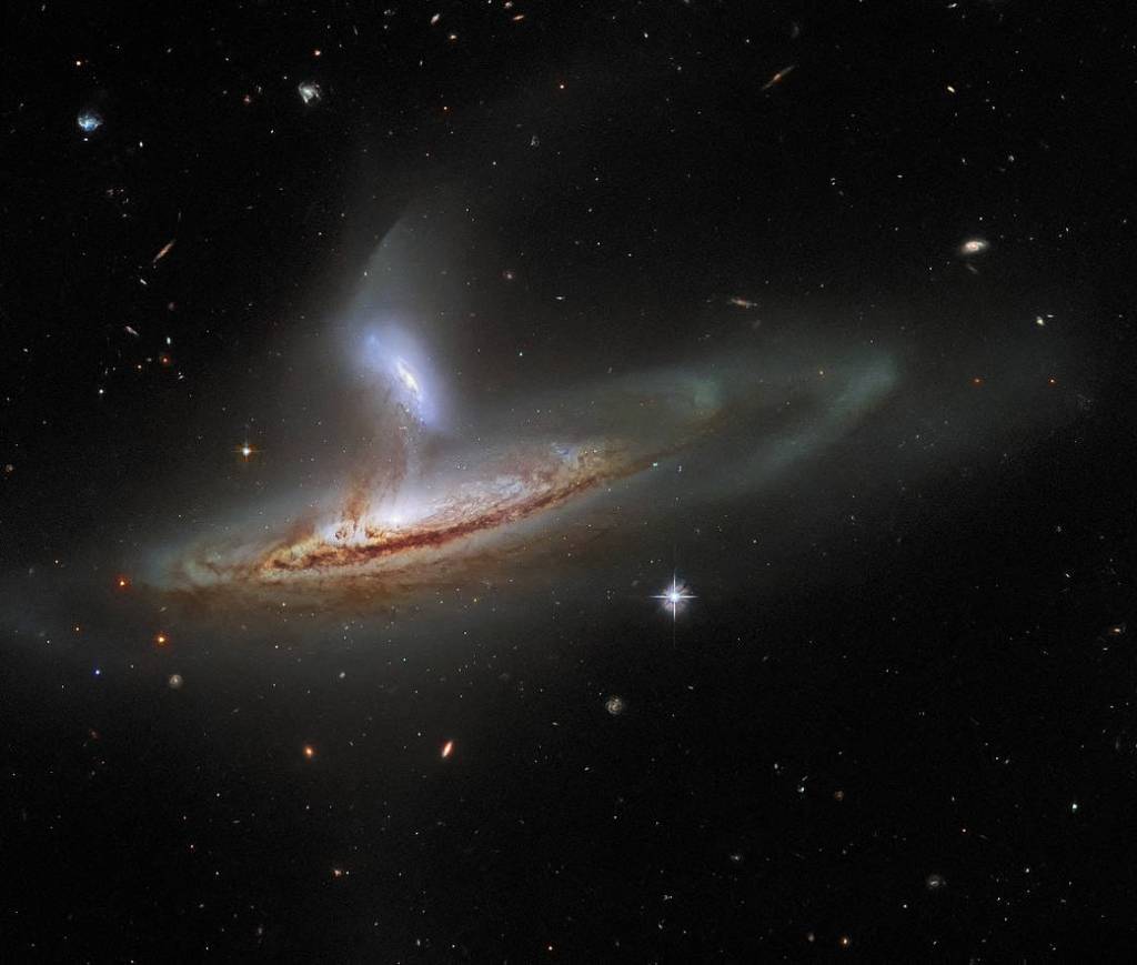 galaxy pair interacting. A nearly edge-on spiral galaxy from left-center to right side of the image. Another galaxy perpendicular and above it. Dust and gas stream between them.