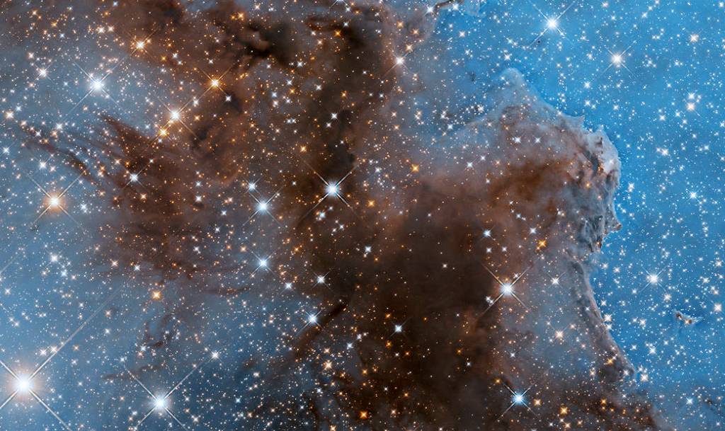 Dark, reddish-brown cloud fills the screen stretching from upper-left to filling the bottom of the image. Blue background is dotted with bright-white and yellow-orange stars.