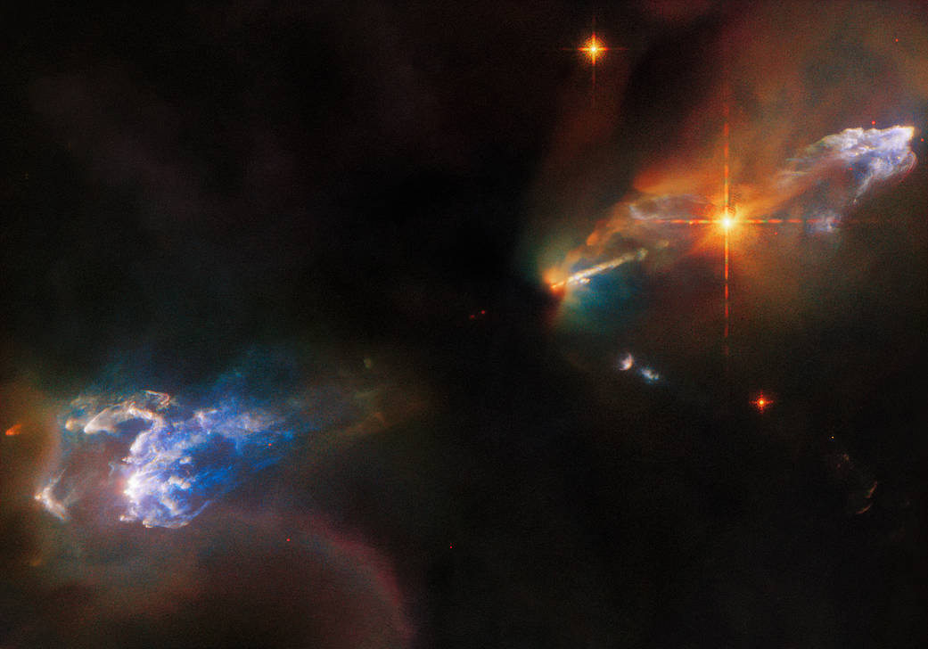 2 wispy, light blue, gas clouds: HH 1 upper right, HH 2 lower left. Both surrounded by dimmer, multi-colored clouds with dark-black background. Very bright orange star lower left of HH 1. Beyond that star, narrow jet emerging from the dark image center.