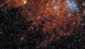 Bright blue-white cluster of stars at upper right, surrounded by field of dimmer stars and rusty-red gas and dust clouds