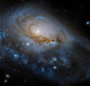 bright spiral galaxy fills the scene. Dark reddish-brown dust lanes bisect the spiral arms. Bright blue stars are dotted troughout.