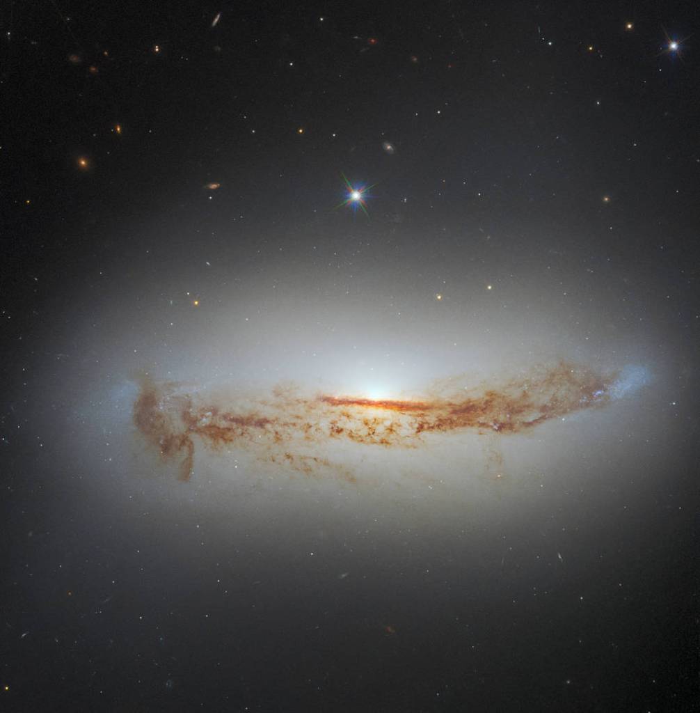 Bright galaxy seen from the side. It has a large central bulge of stars and dust cutting across it lengthwise,