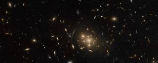 A massive galaxy cluster in the constellation Cetus dominates the center of this image from the NASA/ESA Hubble Space Telescope. This image is populated with a serene collection of elliptical and spiral galaxies.