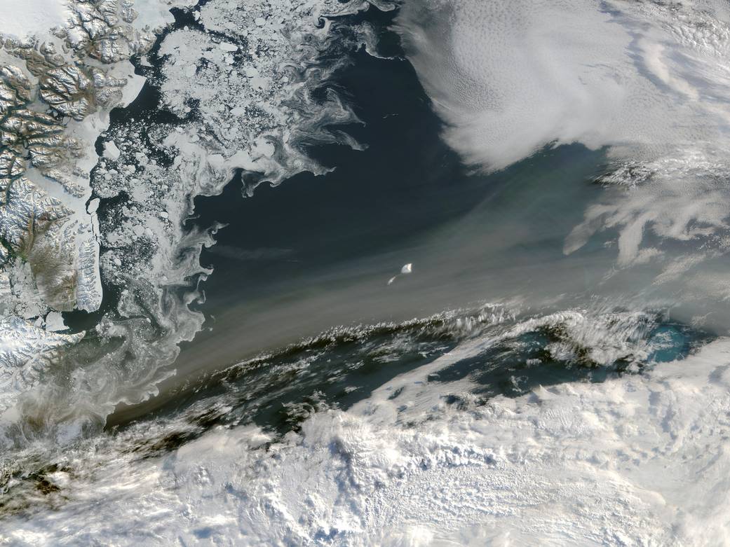 Swirls of gray smoke passing over dark blue water and sea ice on shore