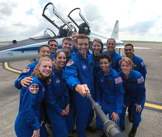 NASA's twelve 2017 astronaut candidates wearing blue flight suits pose for group photo with aircraft in background
