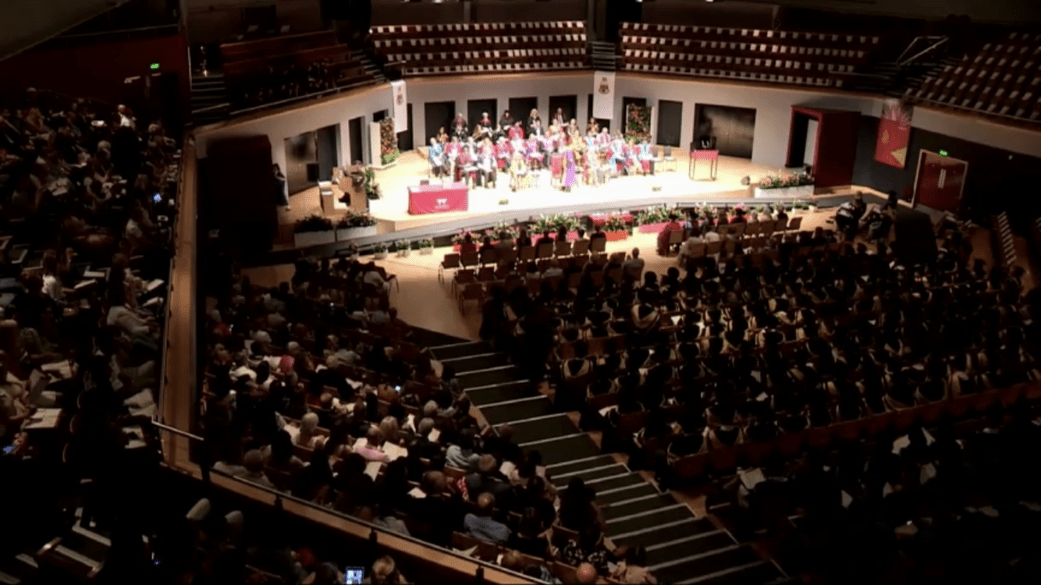 A crowd watches a graduation ceremony in an auditorium