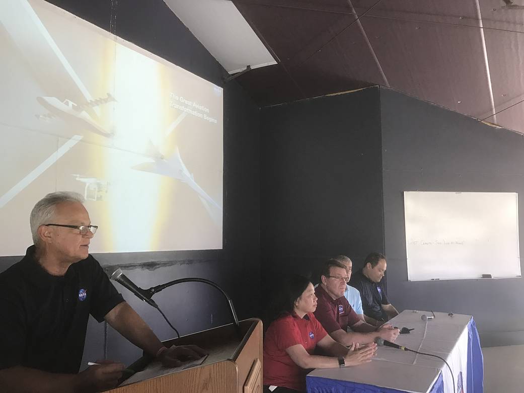 One person standing at a podium and four people seated to his right
