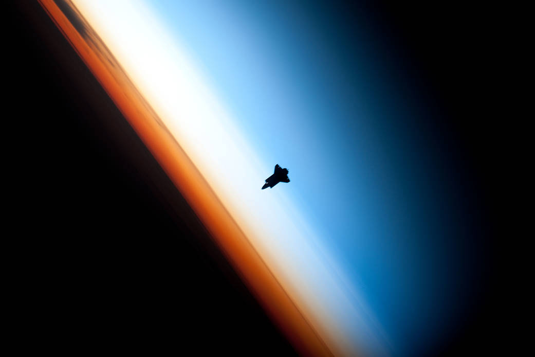 Silhouette of space shuttle against the edge of Earth's atmosphere