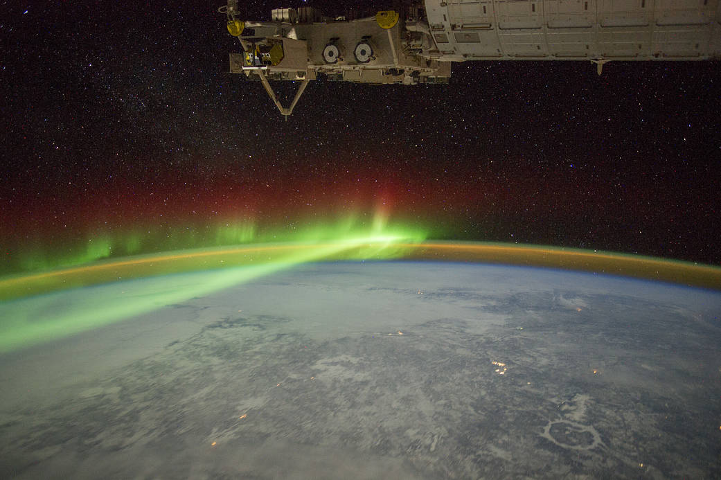 Aurora in brilliant green photographed from orbit with Earth below and crater visible on landscape