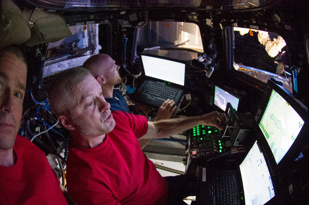 Astronauts inside space station cupola look at computer screens