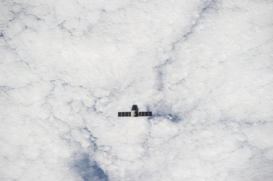 SpaceX Dragon spacecraft in distance with clouds below
