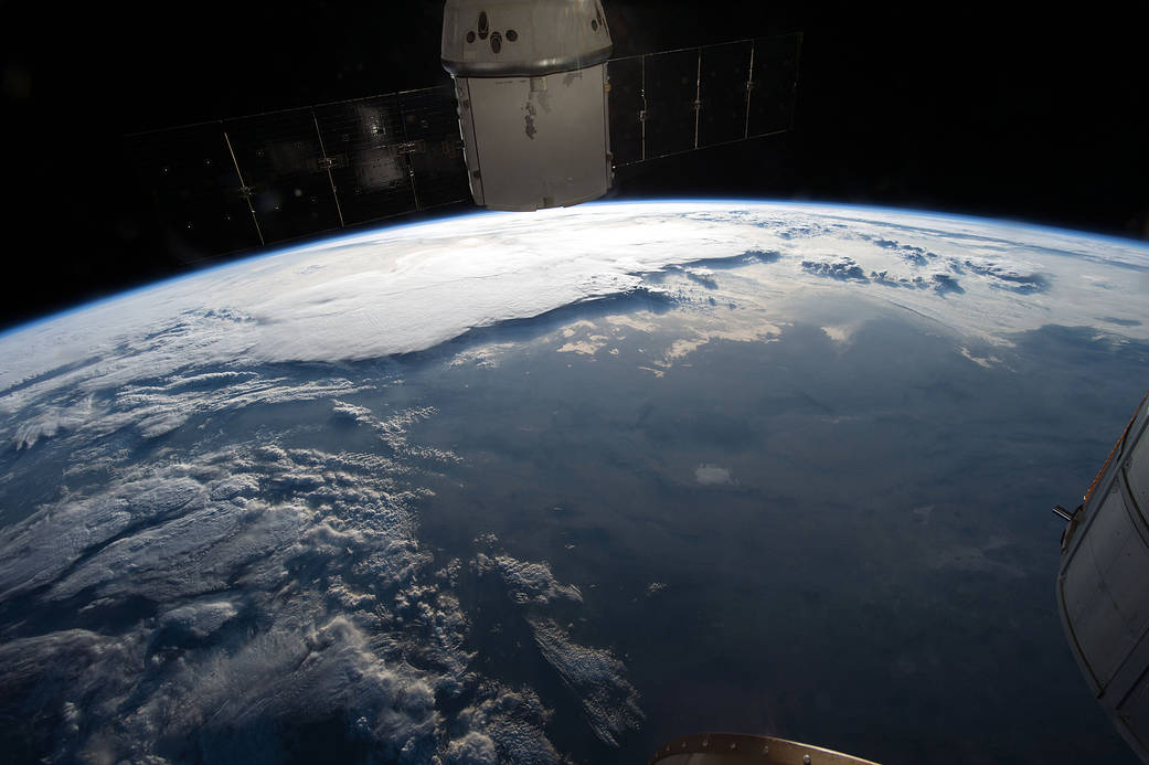 Sunrise over Earth with canyon and clouds below and docked spacecraft at top of frame