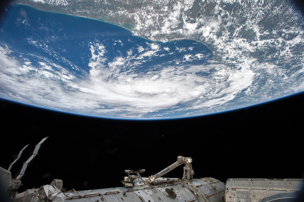Earth from space with tropical storm visible above and space station's robotic arm below