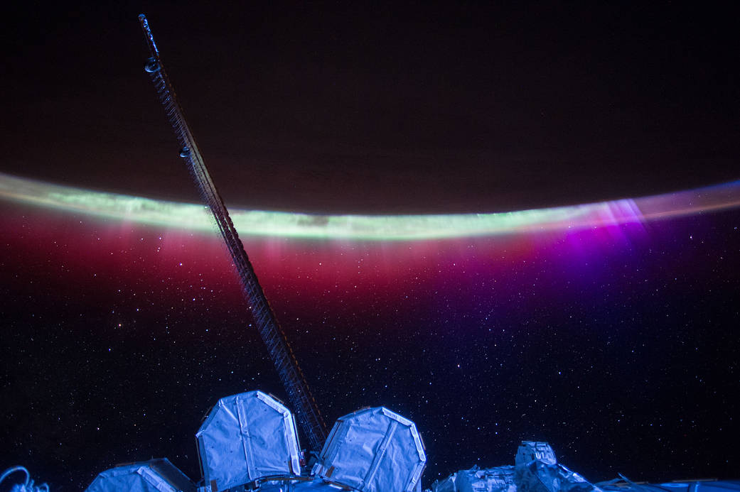 Bright lights of an aurora along the curve of Earth's horizon, photographed from the International Space Station