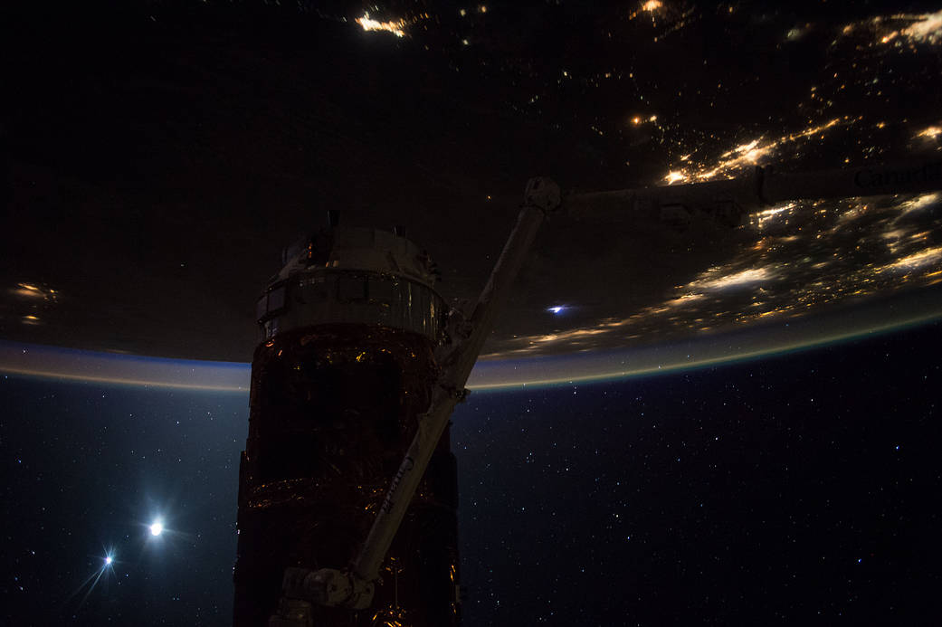 Nighttime photograph of lights on Earth with HTV cargo vehicle on space station in foreground and moon and Venus visible