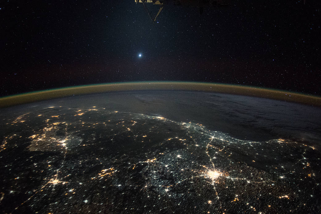 Bright star and planet Venus far off in sky with nighttime city lights of Earth visible below