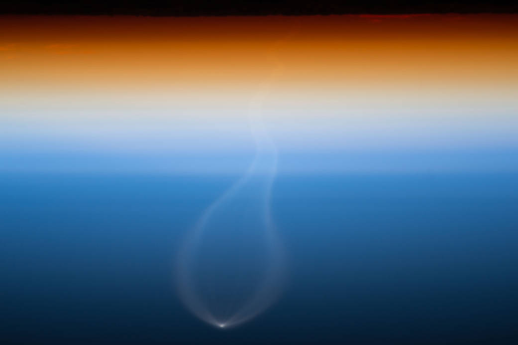 Earth's atmosphere at sunset with bright spot of rocket launch visible below