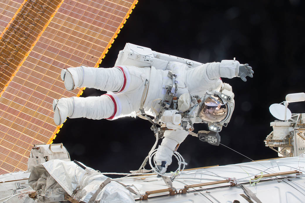 Astronaut in spacesuit on spacewalk with space station's solar array at left of frame