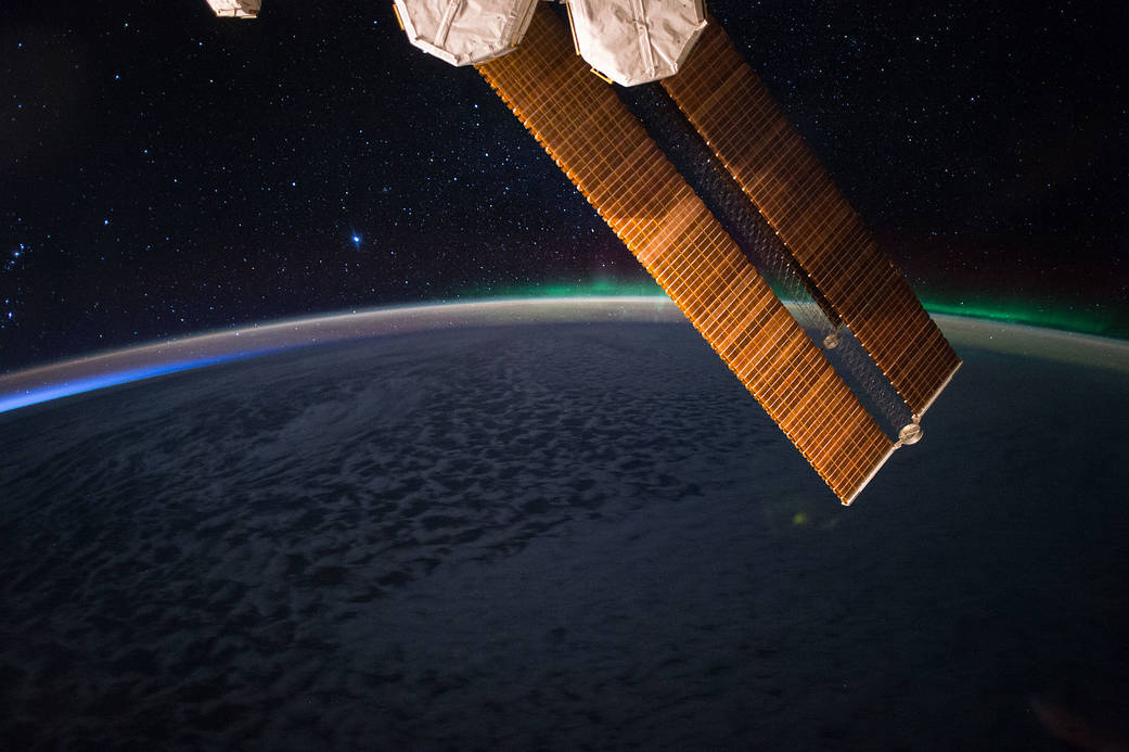 Earth's horizon with aurora and solar array in foreground