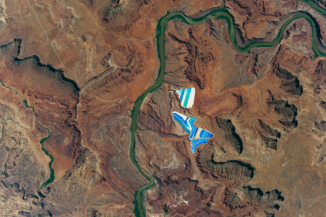 Photograph from orbit of terrain in Utah with small brightly-colored pond just left of center