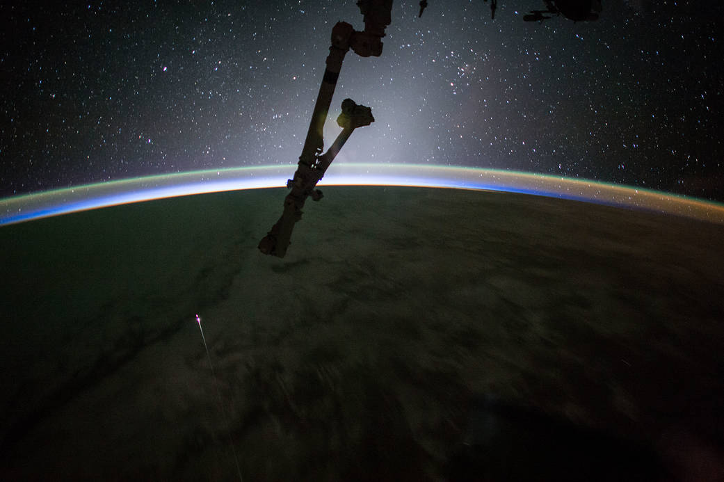Earth's horizon and stars in background with reentering spacecraft visible as small streak of orange