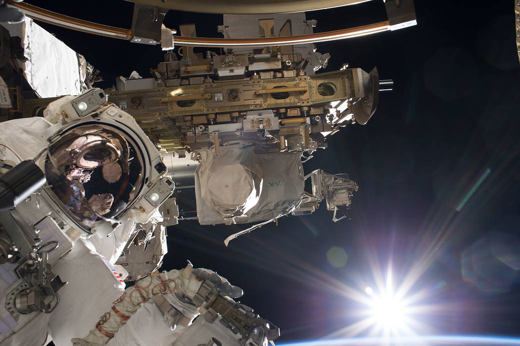 Astronaut in spacesuit at work outside space station module with rising sun in background
