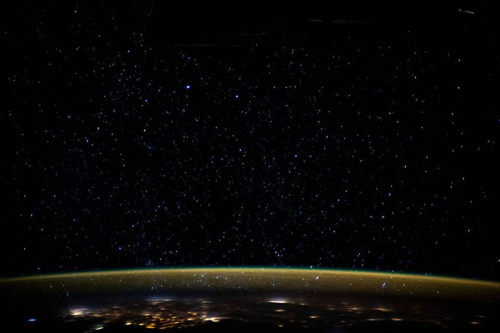 Stars glitter in the night sky above Earth’s atmospheric glow